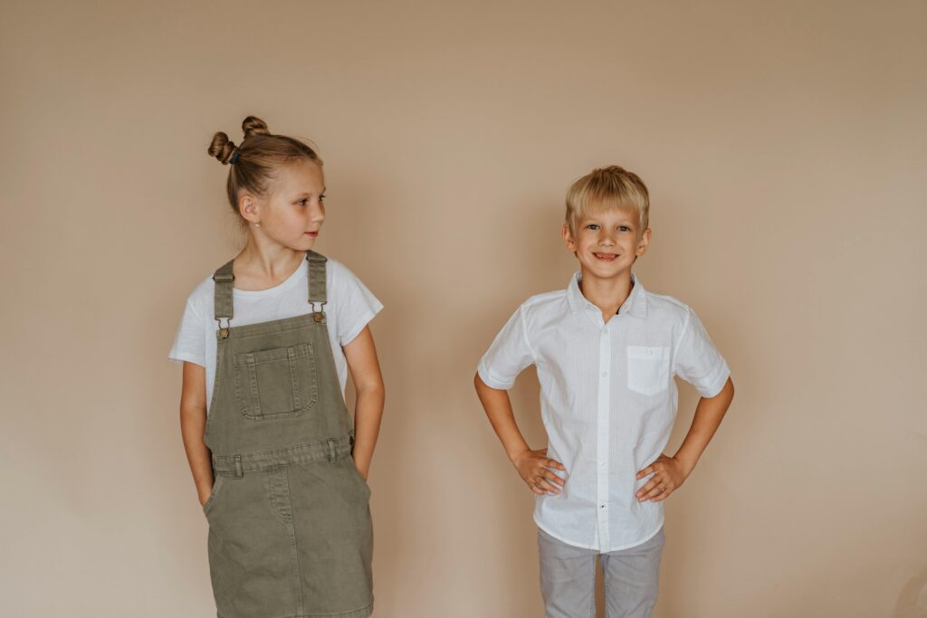 A smiling brother and sister in casual clothing pose against a neutral background.